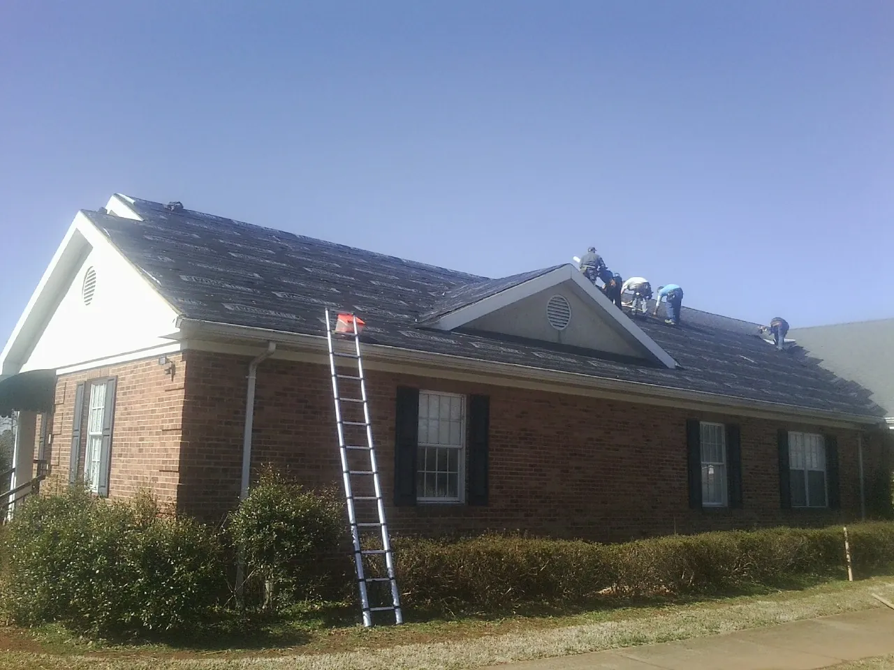 Crew tearing shingles off a brick ranch roof with a ladder set — Metal Roof Repair work by our crew in New Castle