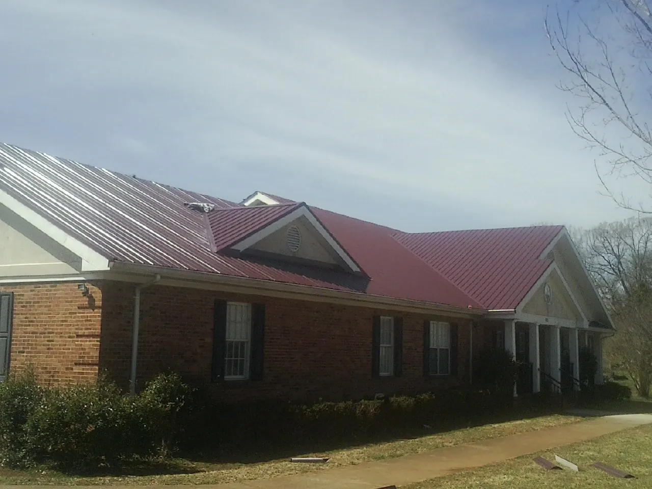 Red metal roof with gabled entries on a long brick building, from a Hail Damage Roof Repair job in New Castle